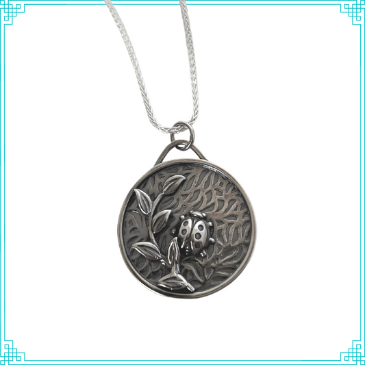 Sleeping Fox handmade silver jewelry created this round pendant with a lady bug and leafy branch elements. The background is a bed of leaves. This pendant hangs from an 18" wheat chain.
