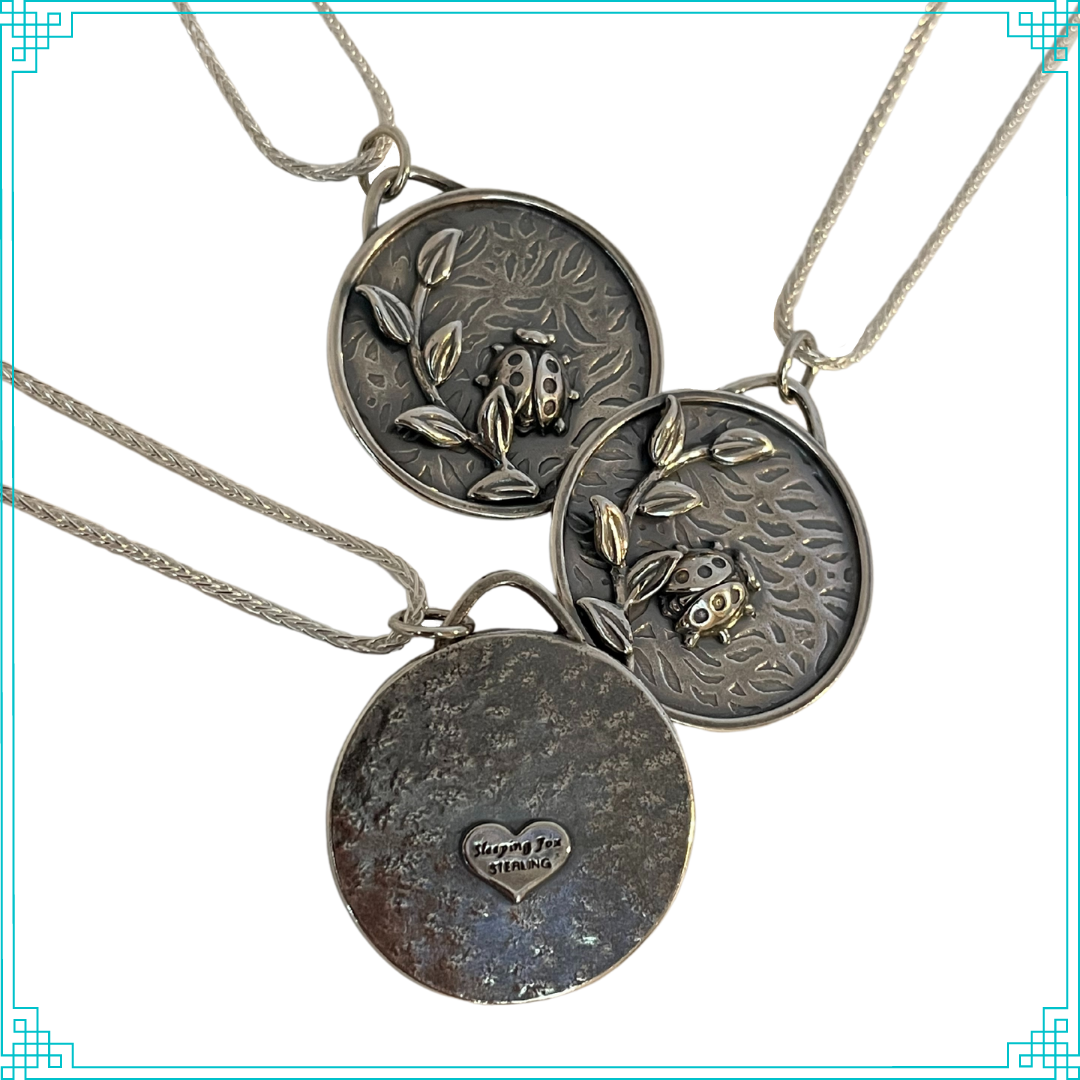 Sleeping Fox handmade silver jewelry created this round pendant with a lady bug and leafy branch elements. The background is a bed of leaves. This pendant hangs from an 18" wheat chain. This photo shows the front and back sides.