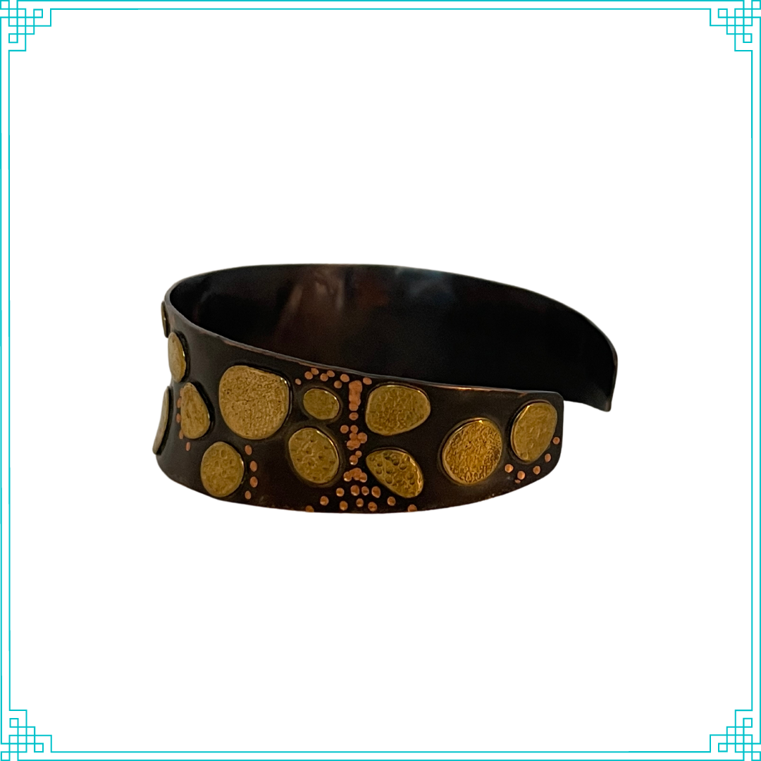 Sleeping Fox quality handmade jewelry presents Nuggets Cuff Bracelet. This bracelet has a wonderful comfort fit due to it's anticlastic shape. Anticlastic means the material has a curve going in two different directions. The base material is copper and the top elements are brass. The whole piece has been given a patina of black and the patina has been polished off the brass. The dot design is done with a ball bur.