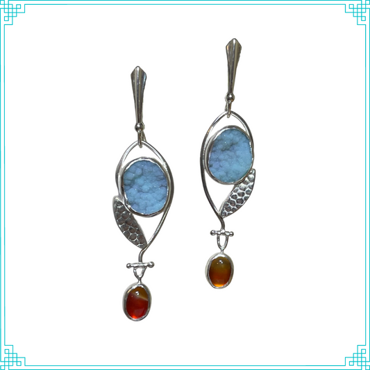 Sleeping Fox handmade silver jewelry presents Bloom earrings. The featured top stone is a bright blue chrysocolla snuggled with a leaf. A carnelion seed swings below a hinge with the breeze.