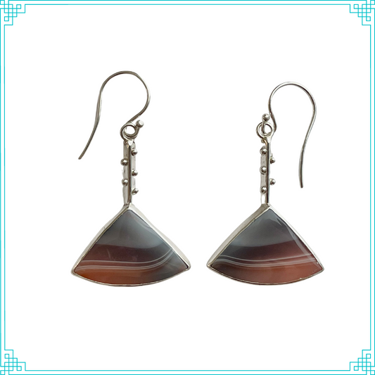 These Sleeping Fox banded agate earrings have a soft pallet with smokey blue lines fading into a hazy light peach color. Truly remarkable! The stones hang from a triangle wire studded with sterling silver balls. On the back, the hallmark sits upon distinctive curved lines resemble tree rings. We hand make the sterling ear wires.  