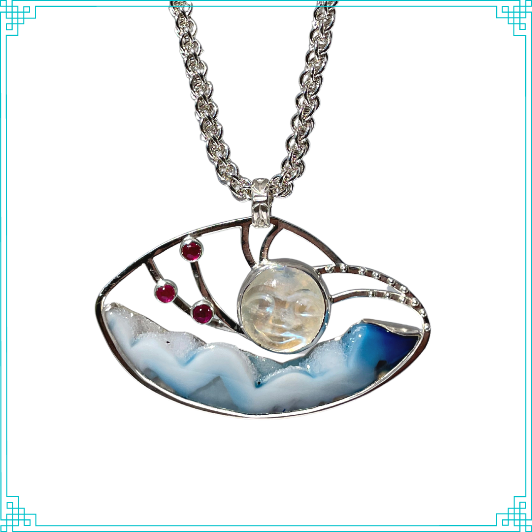 This original quality Sleeping Fox design shows off a Brazilian Agate of blue with white drusy.  The carved rainbow moonstone face (man in the moon) is just above the clouds with red ruby planets and little silver stars keeping him company. The "Jens Pind" sterling chain is hand made by Bev and is made to be worn at two lengths 16" & 18". 